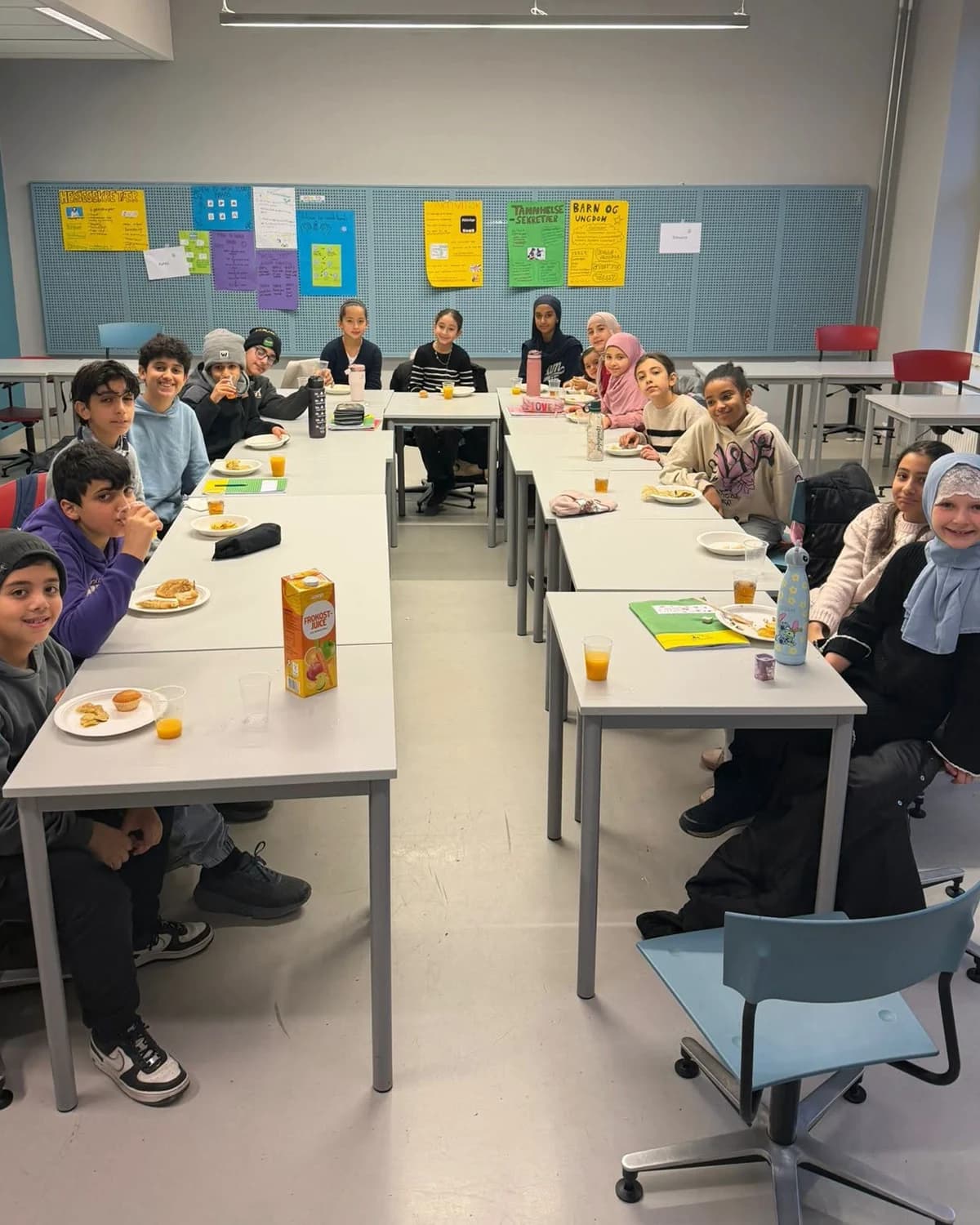 Pupils at Rabita school around the tables at breakfast, their classroom posters on the wall behind